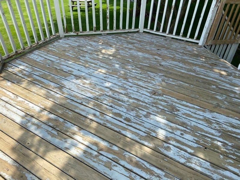 Weathered wooden deck with peeling white paint and green grass in the background.