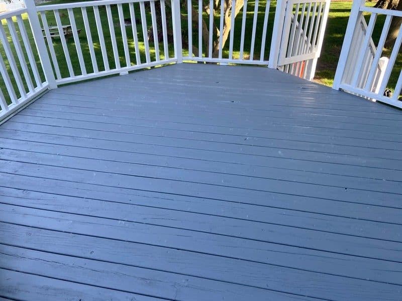 Freshly painted gray wooden deck with white railings in a backyard setting.