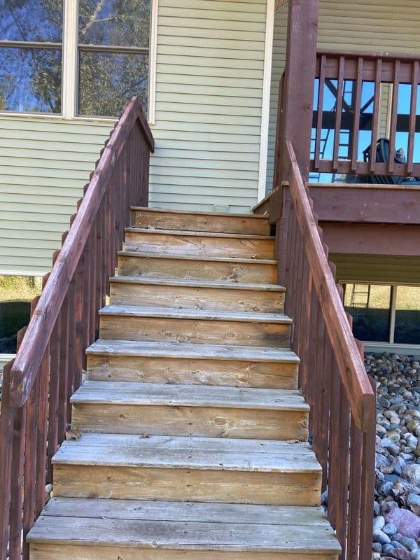 Wooden stairs leading up to a house with a green siding and a balcony railing.
