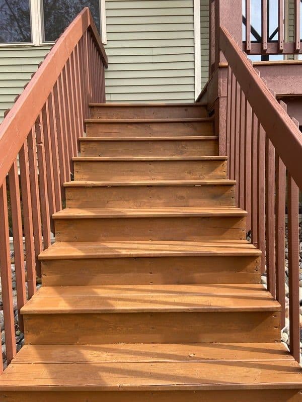 Wooden steps leading up to a home with a railing and a view of the porch above.