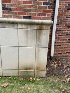 Dirty exterior wall with stains near a brick building and grass area.