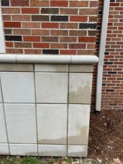 Water-stained stone wall adjacent to brick building, showing texture and color contrast.