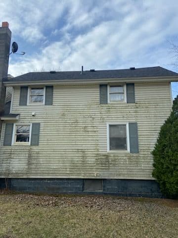 Two-story house exterior with weathered siding and green shutters under a cloudy sky.