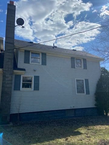 Side view of a two-story house with a chimney, satellite dish, and clear blue sky.